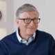 A man with glasses sitting in front of a clock.