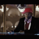 A man in a suit and red hat is sitting at the bar.