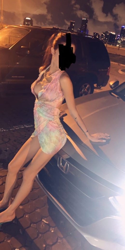 A woman in a dress standing next to a car.